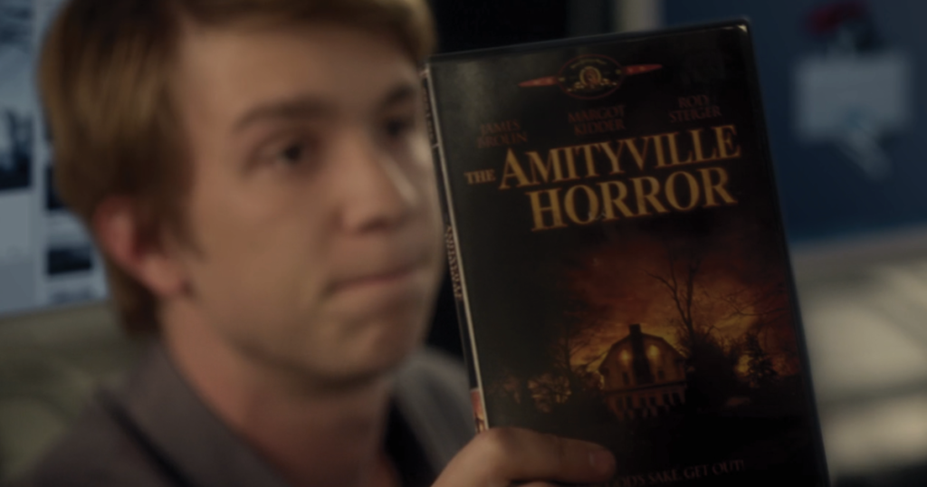 A screenshot from Amityville: The Awakening showing one of the teens proudly displaying the DVD for the Amityville Horror remake with Ryan Reynolds.